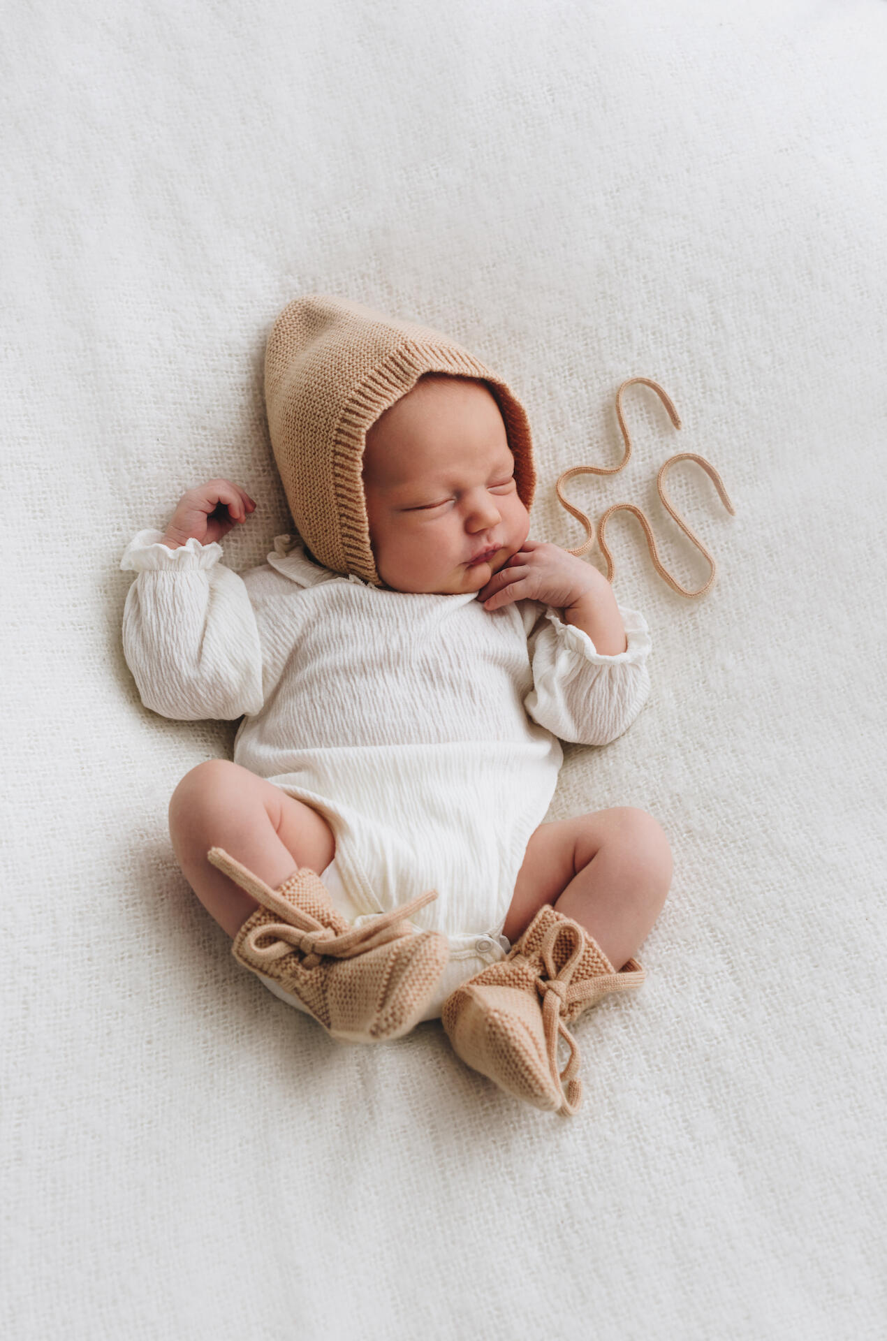 Sesja noworodkowa – Anna Janowska Sesja noworodkowa w studio w Krakowie – śpiące niemowlę w jasnej owijce, fotografia Anny Janowskiej